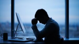 Man with his head in his hands in a dark office, sitting at his desk