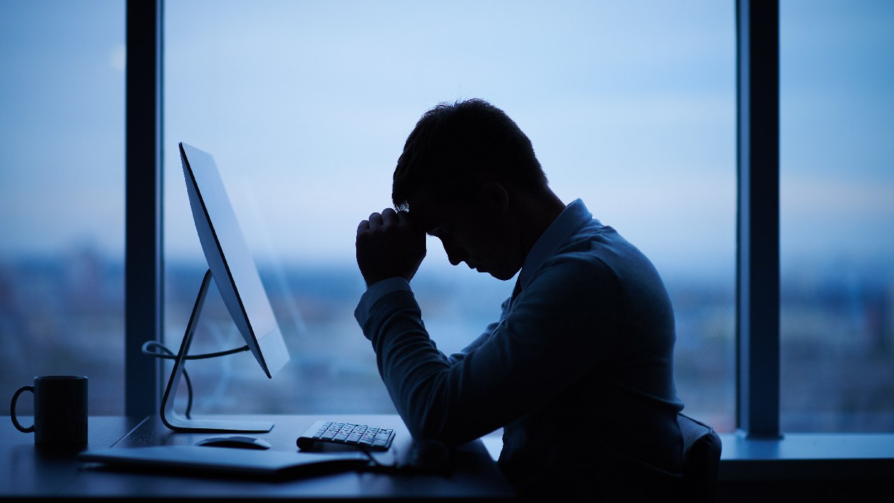 Man with his head in his hands in a dark office, sitting at his desk