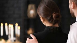 man and women standing at funeral in front of candles