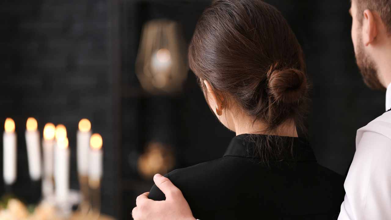 man and women standing at funeral in front of candles